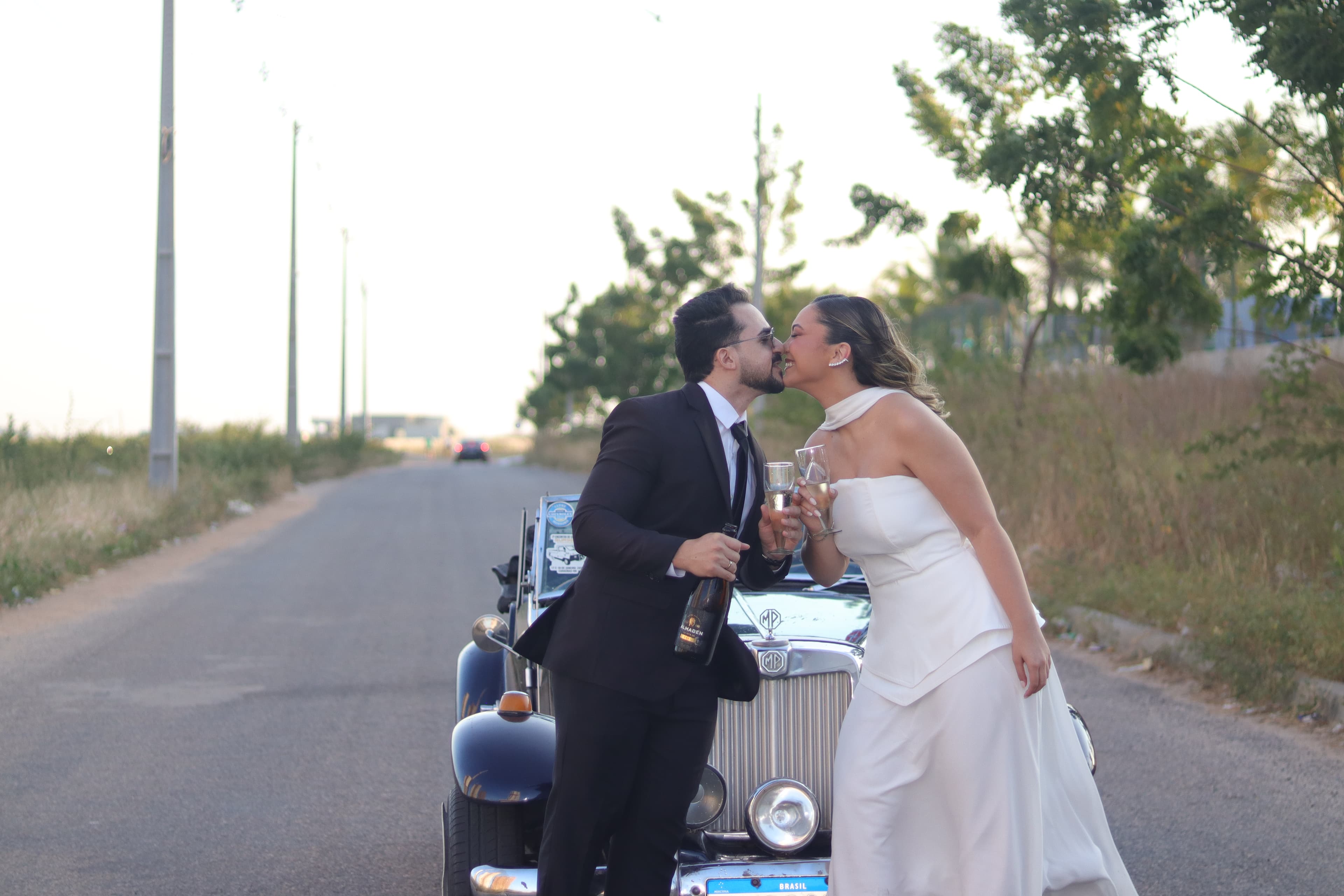 Imagem de Gabrielly e Rellyson em frente a um carro MG azul comemorando e sorrindo um para o outro.